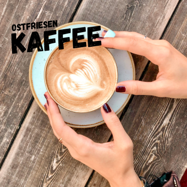 Tasse Ostfriesentee mit Herz-Milchschaum auf einem Holztisch.
