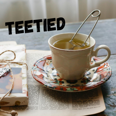 Tasse mit Tee, Sieb und buntem Unterteller auf einem Tisch mit Buchseiten.