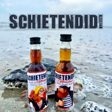 Zwei Flaschen Schietendidi auf einem sandigen Strand, im Hintergrund der Himmel und das Meer.
