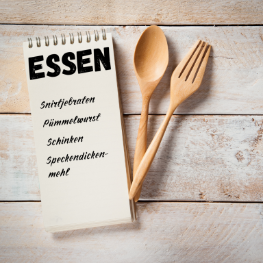 Notizblock mit der Überschrift "ESSEN" und Holzlöffel sowie Gabel darauf.